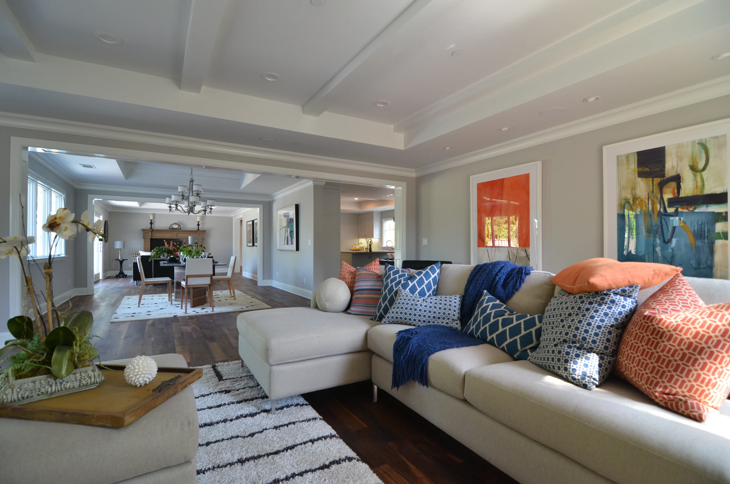 A white sectional with orange and blue cushions looking toward a dining area