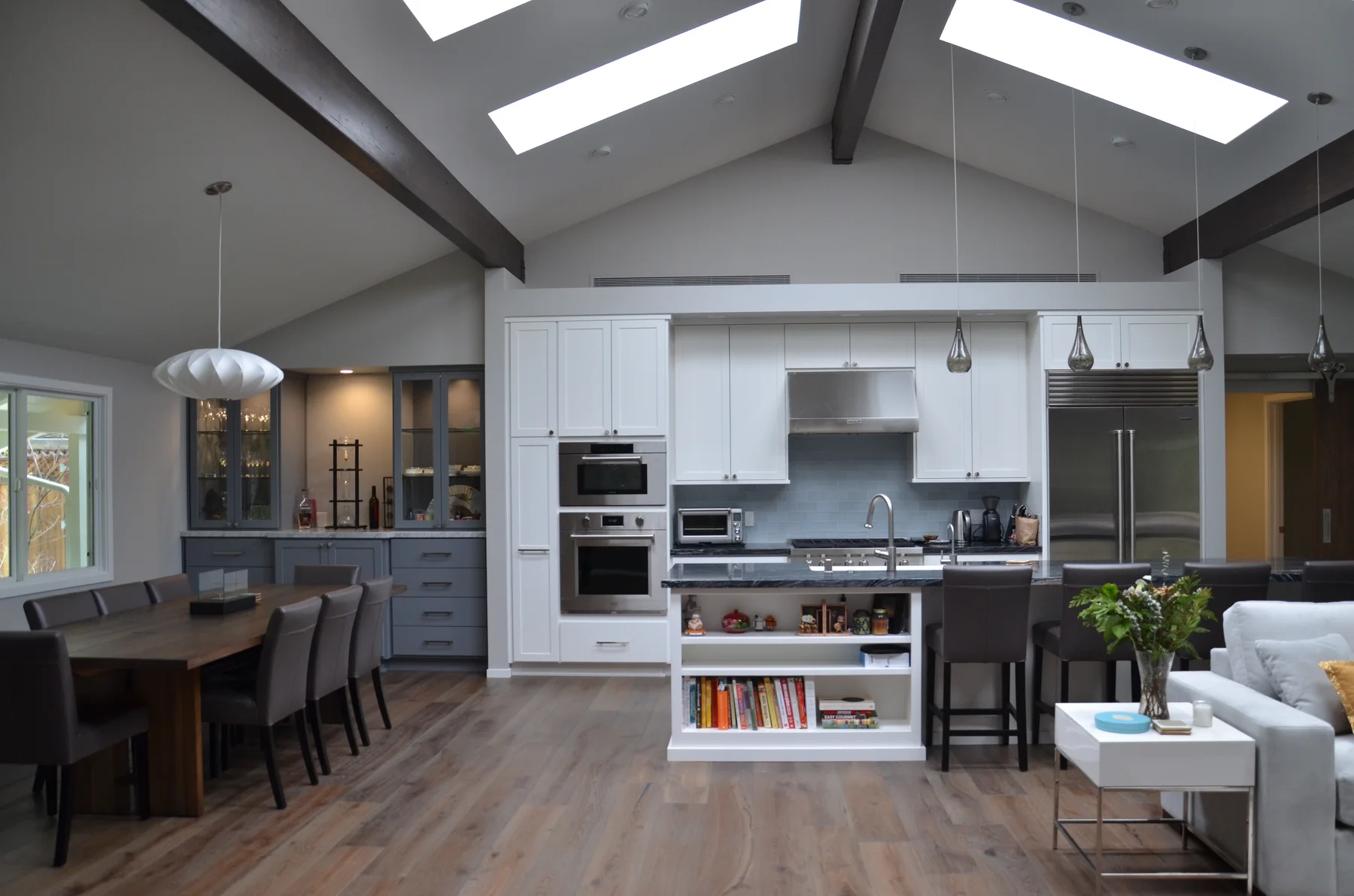 Open kitchen and dining room with skylights, dark ceiling beams, and white cabinetry