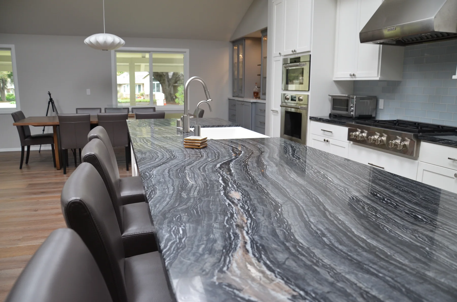 White kitchen with a dramatic gray stone island and dark leather stools