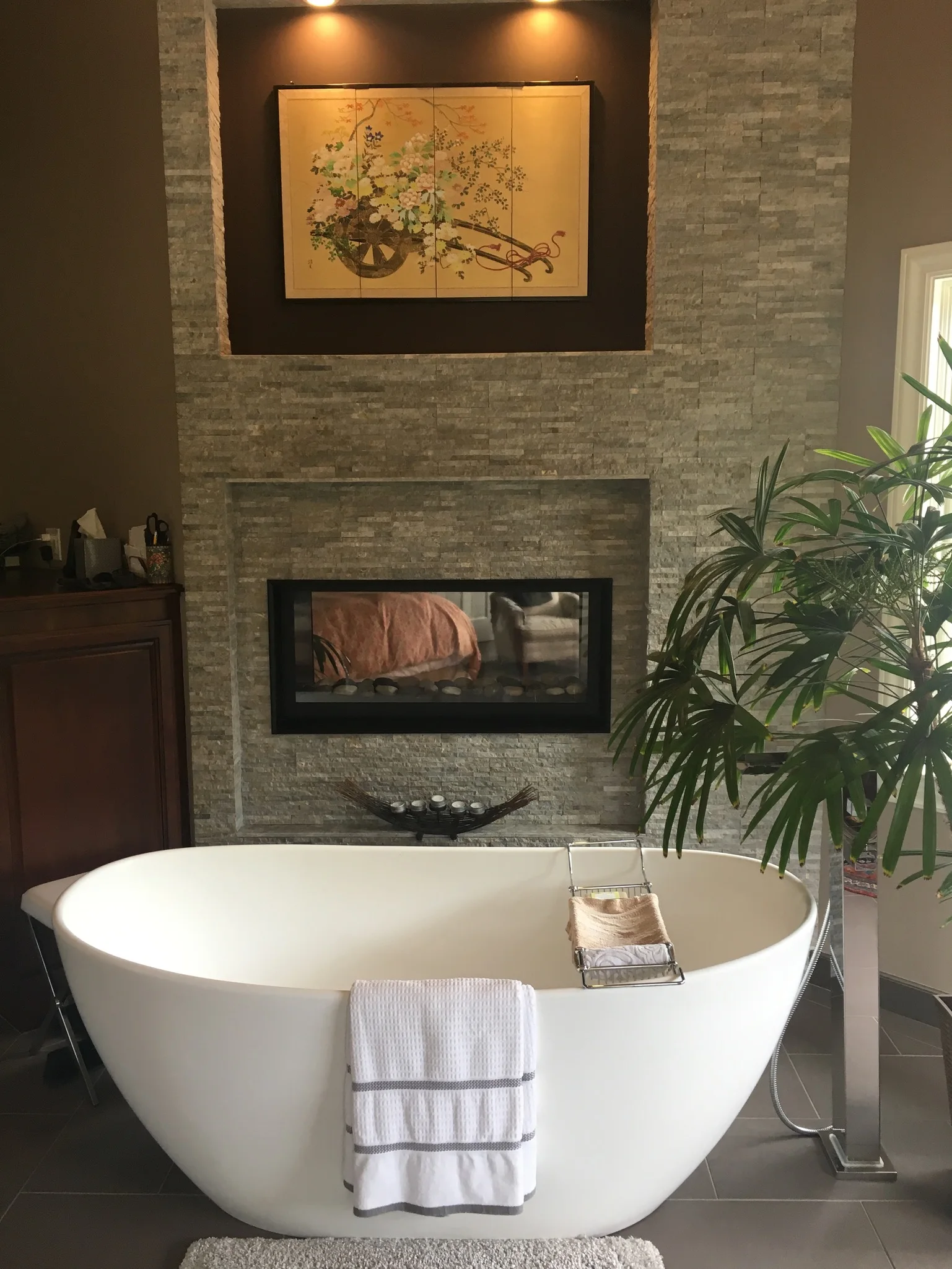 Freestanding bathtub beside a stone fireplace and leafy plant