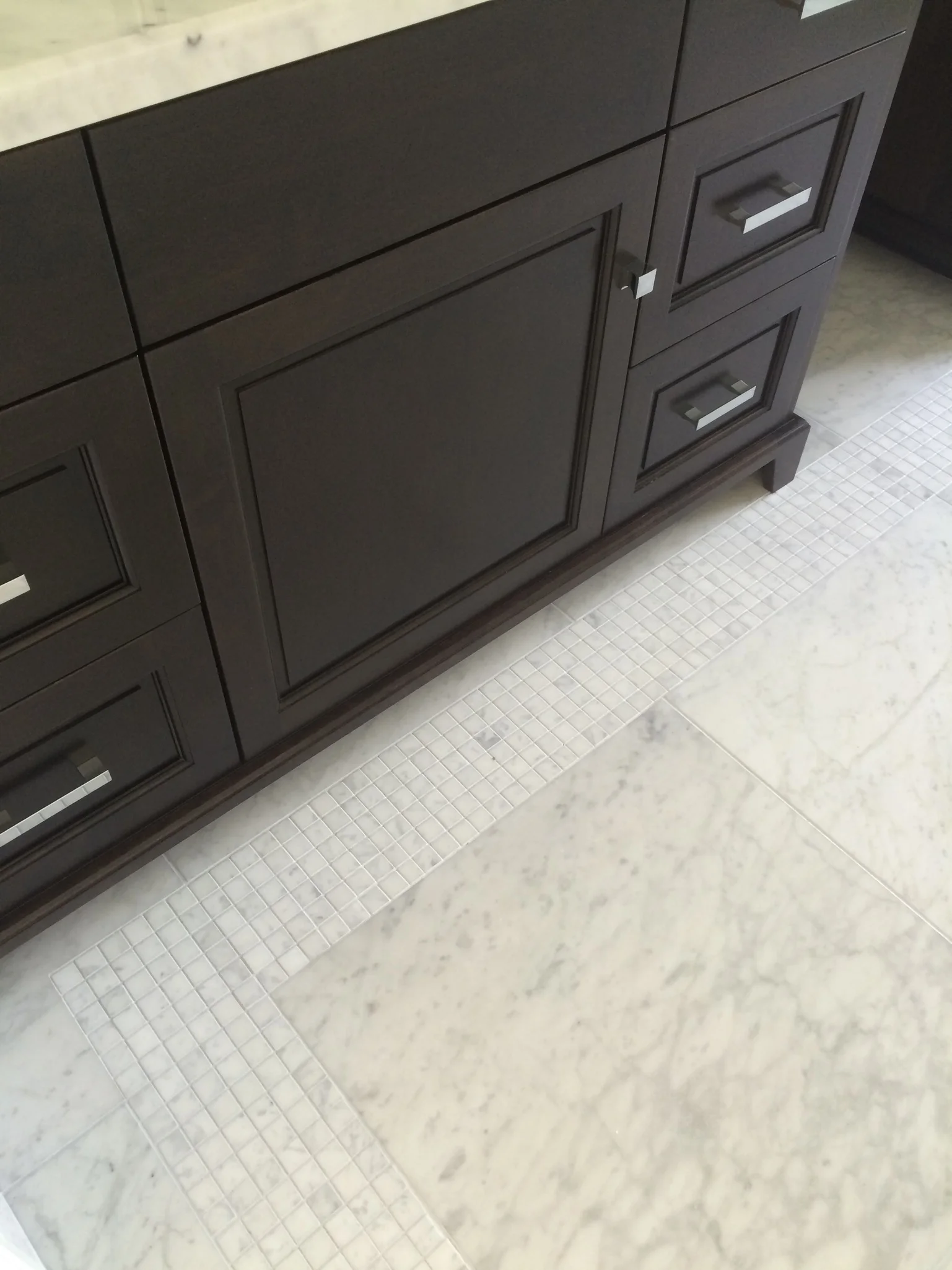 Dark bathroom vanity with a pale marble mosaic floor