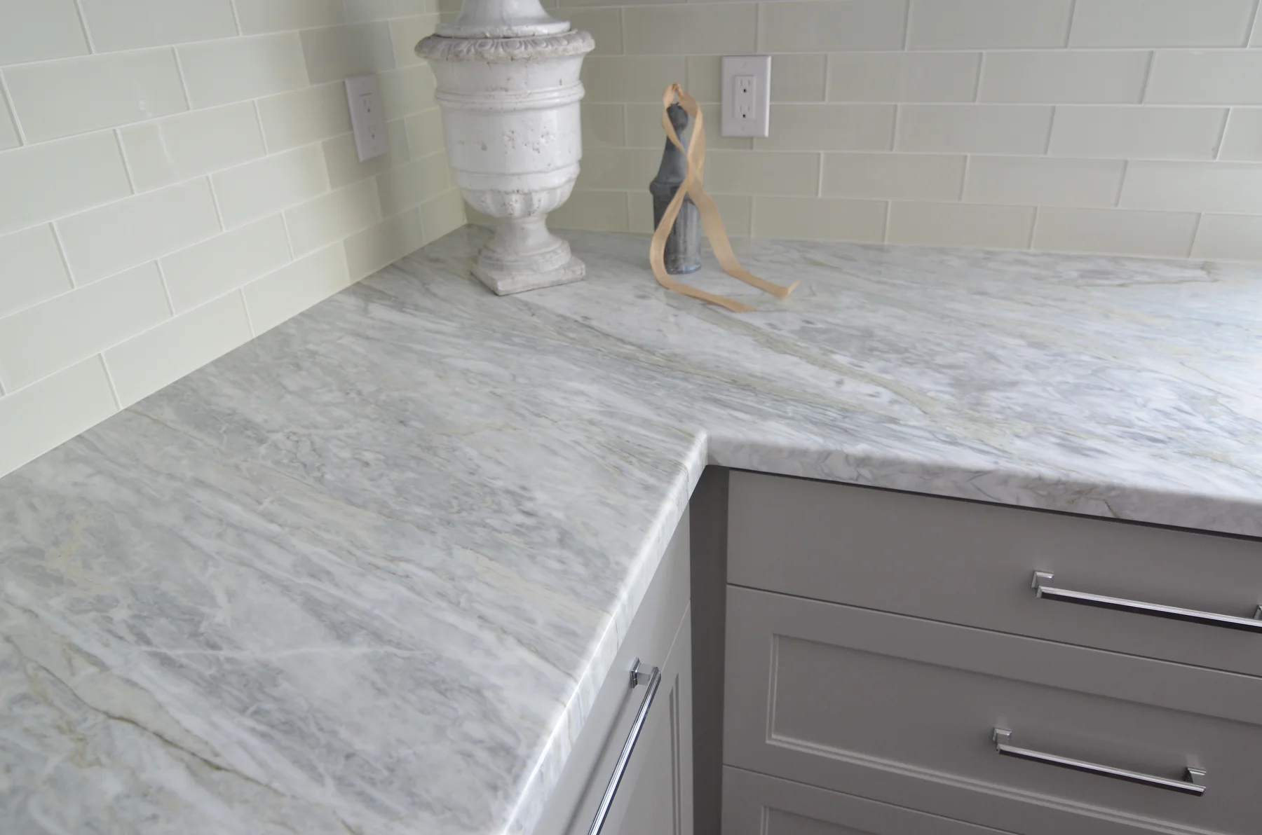 Pale stone bathroom counter with gray cabinetry and glass tile