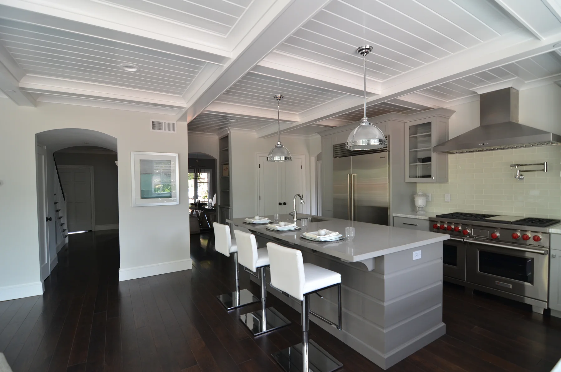 Gray kitchen with a coffered ceiling, white stools, and pendant lights
