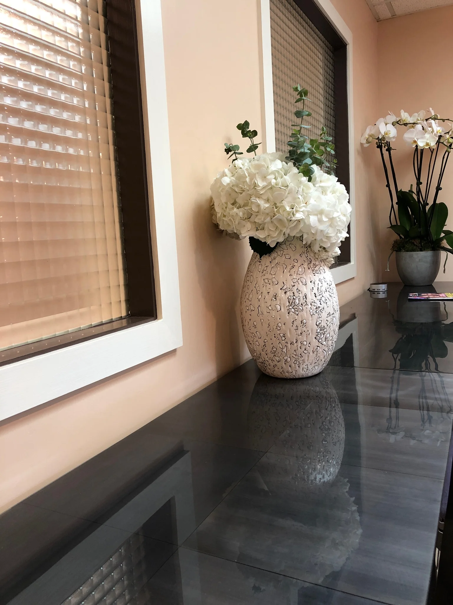 White flowers in a textured vase on a glossy black surface